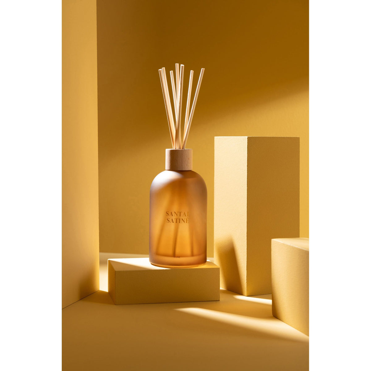 Geurstokjes Accords Essentiels Santal Satiné 250ml van J-Line op decoratieve blokken in een warme sfeerfoto